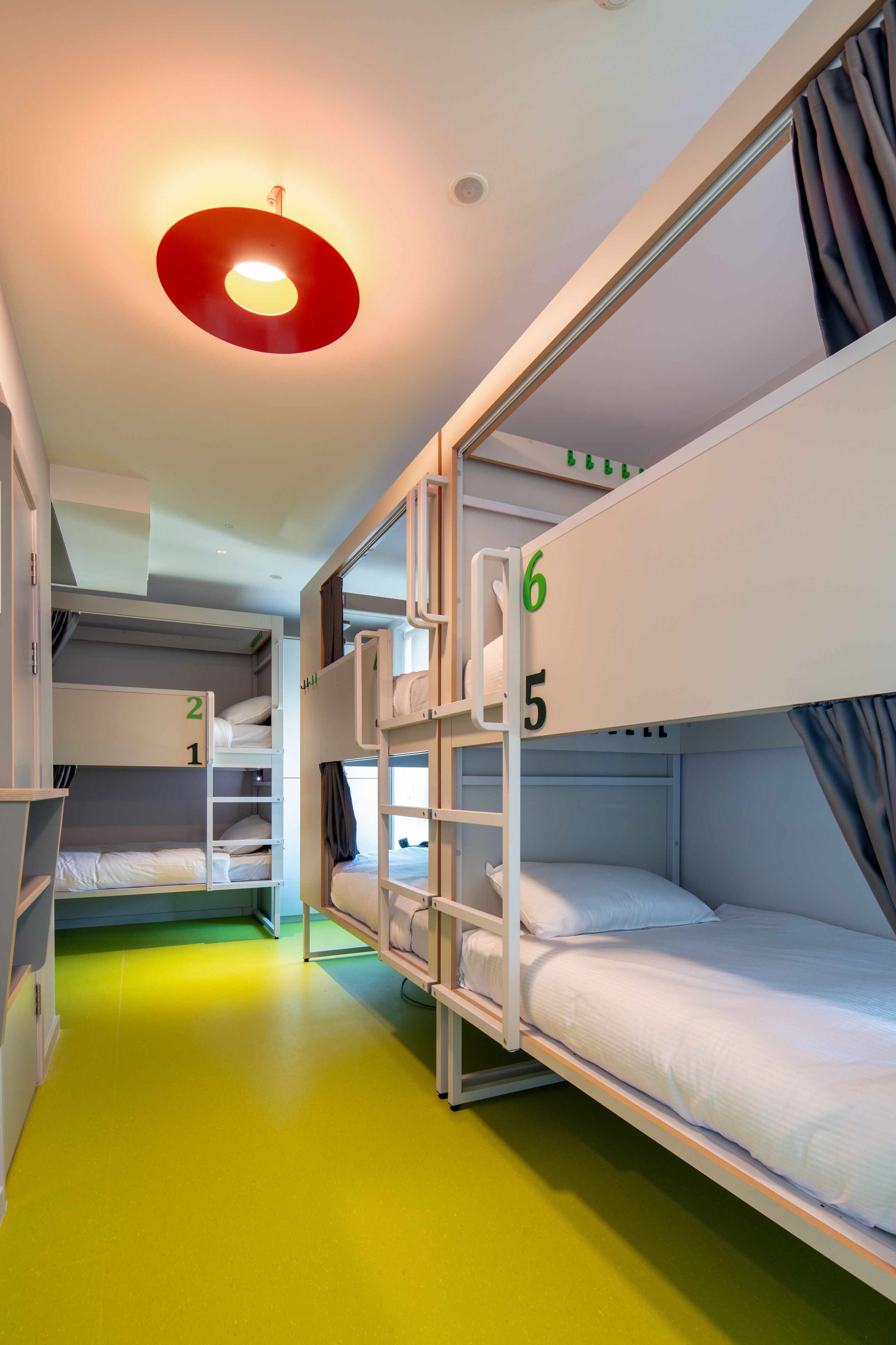 A bunk room with bunk beds numbered 1 to 6, a red ceiling light, and a green floor.