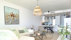 Ein modernes Wohnzimmer mit einem weißen Sofa, einem Essbereich und einer Küche im Hintergrund.