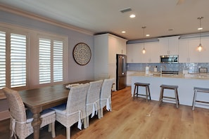 A modern kitchen with a wooden dining table, wicker chairs, a refrigerator, a microwave, and pendant lights. - Bayside Breeze | Pool + Water Views! (Gulf Shores)
