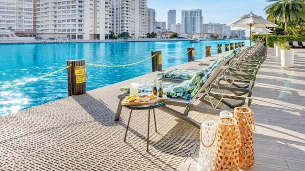 Ein Poolbereich mit Liegestühlen, einem Tisch mit Snacks und Blick auf hohe Gebäude.
