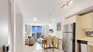 Eine moderne Küche mit einem Edelstahl-Kühlschrank, ein Essbereich mit Tisch und Stühlen sowie ein Blick auf die Stadt durch große Fenster.