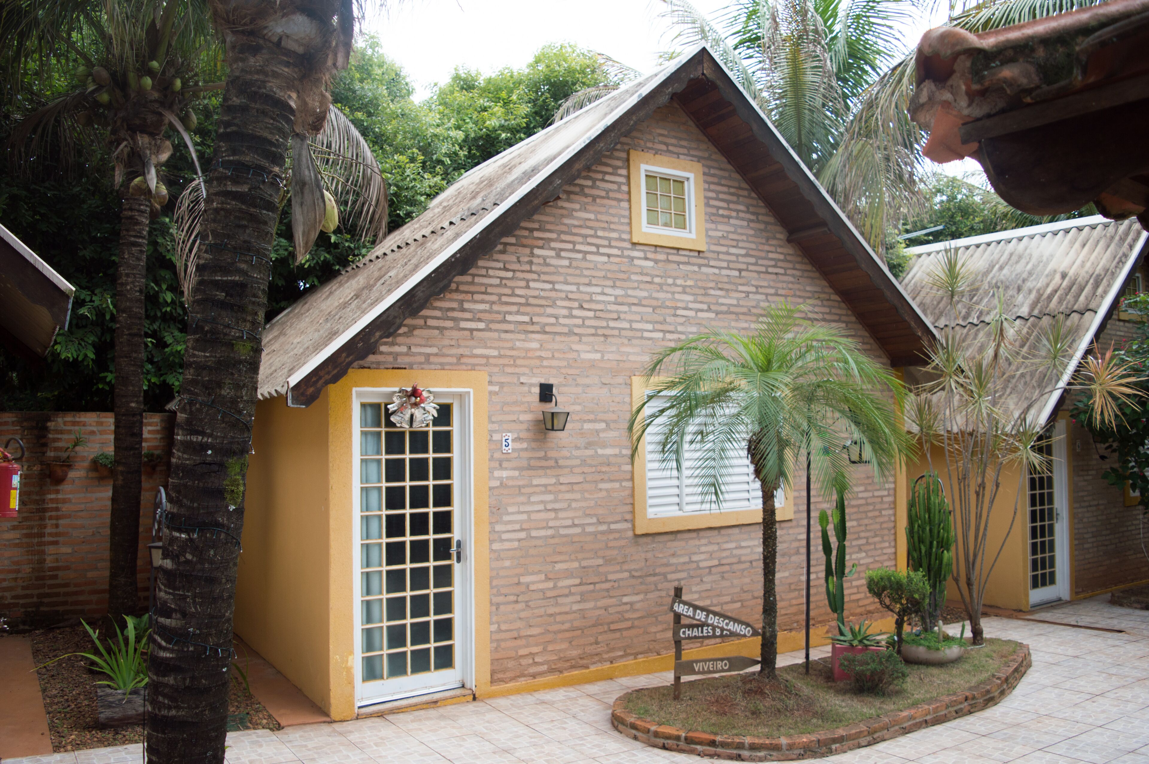 Un petit bâtiment en briques avec une porte et une fenêtre jaunes, entouré de palmiers et de plantes.
