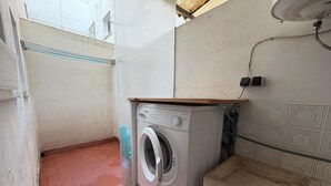 Een praktische wasruimte met een wasmachine, een klein wastafeltje en een betegelde muur.