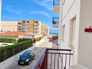 A residential street with a car parked on the side, buildings with balconies, and a clear sky. - WIMPY esc.B 1º  Solo Familias! (Xeraco Playa)
