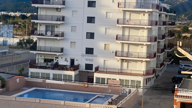 Een hotel met meerdere verdiepingen, balkons, een zwembad en een bergachtige achtergrond.
