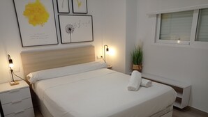 A neatly made bed with white linens, a bedside table with a lamp, and a wall with framed artwork.