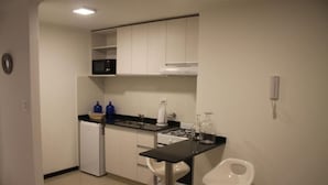 A compact kitchen with white cabinets, a microwave, a small refrigerator, a gas stove, and two white stools. - Boulevard Illia 10C (Córdoba)