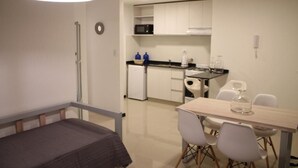 A compact room with a bed, a dining table with chairs, a kitchenette, and a ceiling light. - Boulevard Illia 10C (Córdoba)