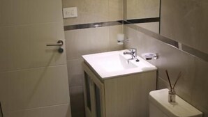 A compact bathroom with a toilet, sink, and shower. - Boulevard Illia 10C (Córdoba)
