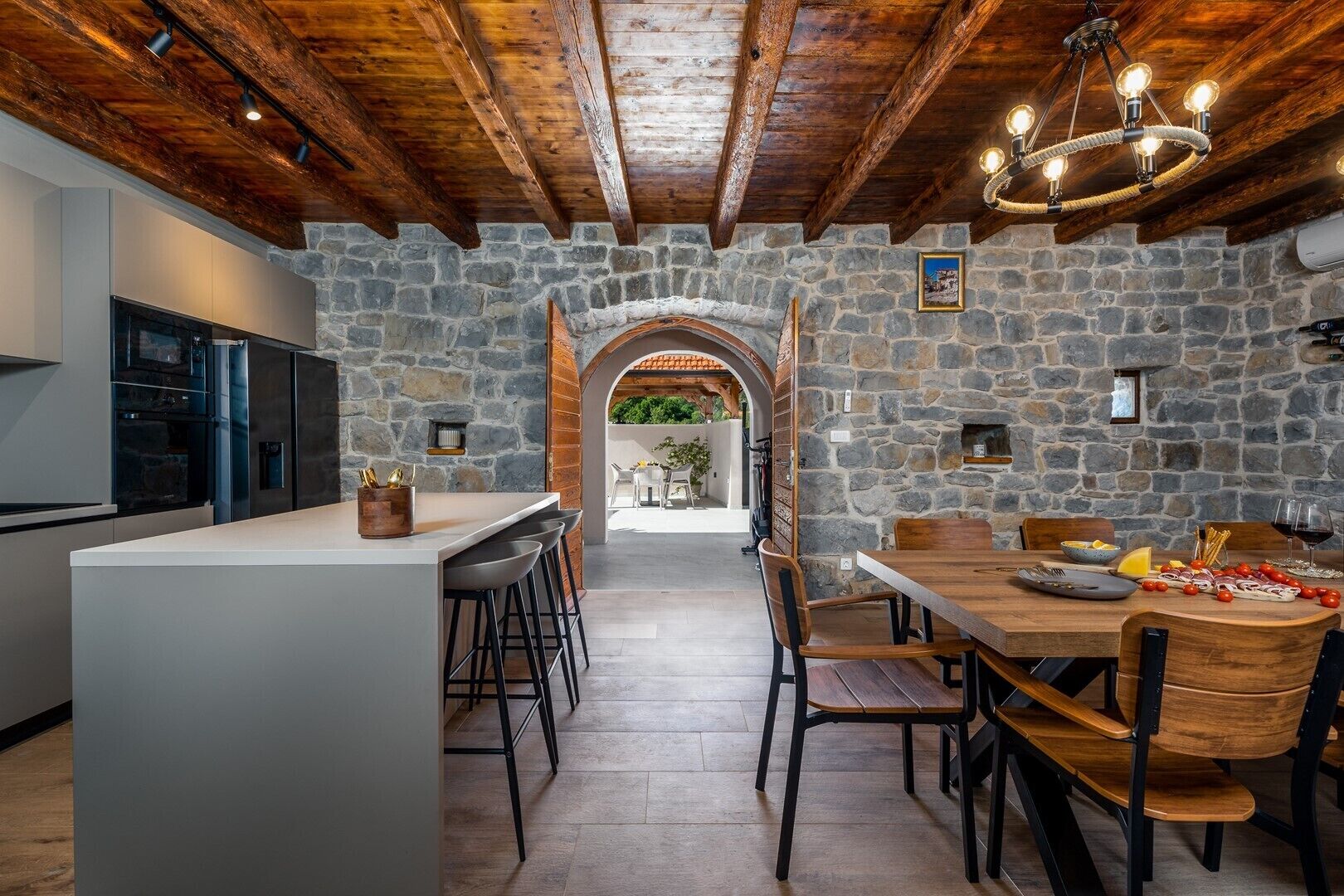 A modern kitchen with a stone wall, wooden beams, and a central island with bar stools.