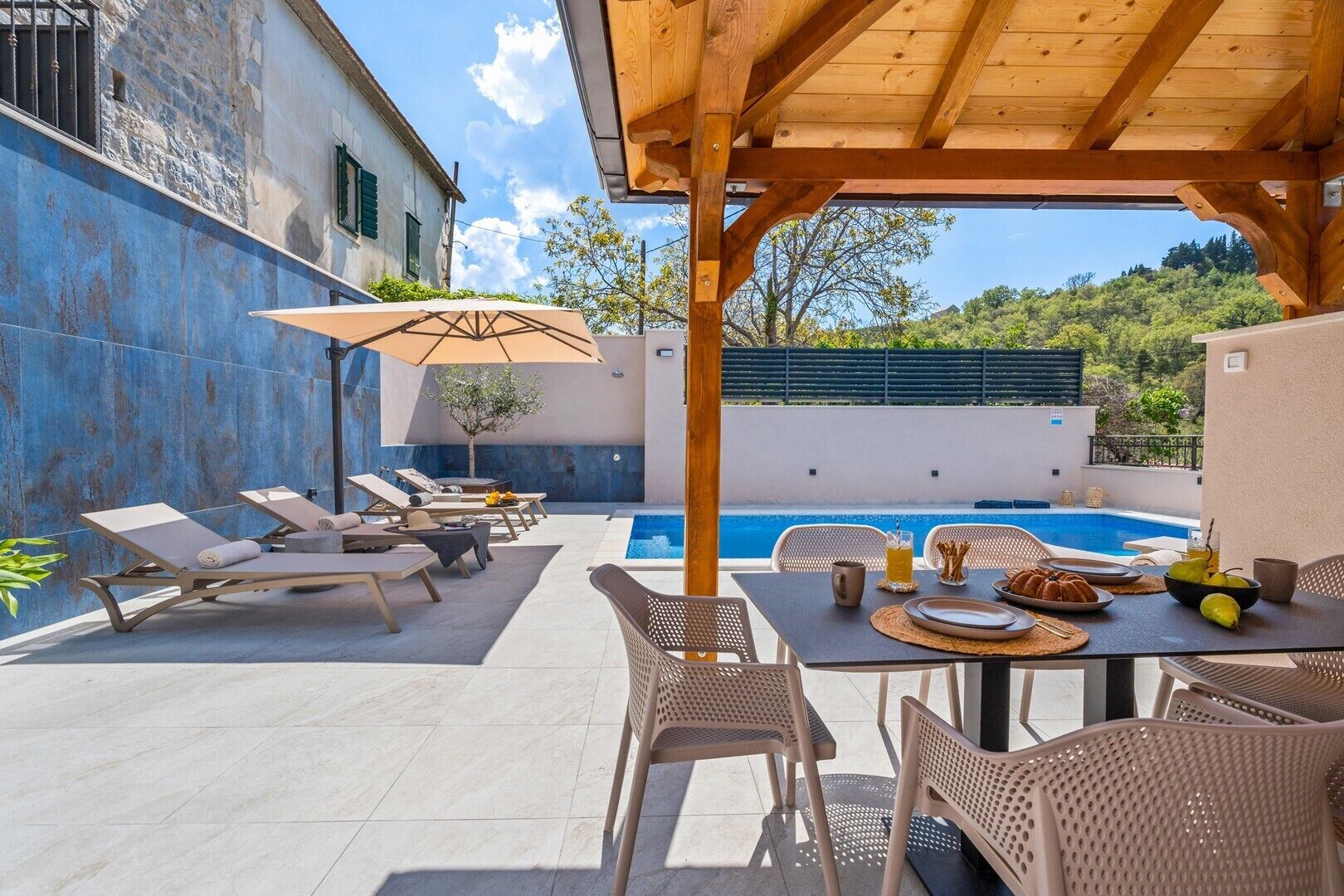A poolside area with lounge chairs and a table set for dining, overlooking a swimming pool.