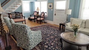 A living room with a staircase, a dining area with chairs, a sofa, a coffee table, and a rug. - Comfortable Home 3 blocks from the beach at the Jersey Shore (Belmar, North end) (Belmar)