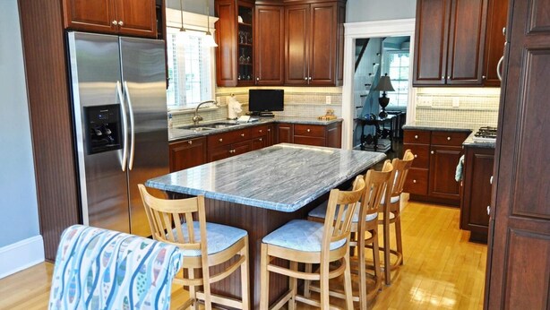 A modern kitchen with dark wood cabinets, a stainless steel refrigerator, a marble island, and wooden chairs. - Comfortable Home 3 blocks from the beach at the Jersey Shore (Belmar, North end) (Belmar)