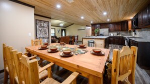 A wooden dining table set with plates, glasses, and cutlery, surrounded by wooden chairs. - Pinot Noir 3 bedroom cabin (BROKEN BOW)