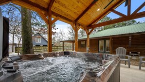 A hot tub area with wooden beams, a covered patio, and a view of a house in the background. - Pinot Noir 3 bedroom cabin (BROKEN BOW)