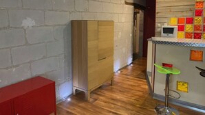 Een kamer met bakstenen muren, een houten kast, een rode opbergunit en een barruimte met kleurrijke tegels en een televisie.