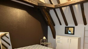 Een slaapkamer met een bed, een klein nachtkastje, een spiegel en een kledingkast.