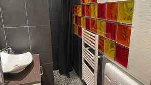 Een badkamer met een wit wastafel, een douche met een zwart gordijn en een betegelde muur met kleurrijke glazen tegels.