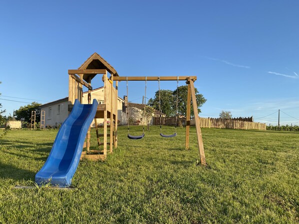 A wooden play structure with a slide and swings in a grassy yard.