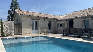 A poolside area with a stone building, outdoor seating, and a clear blue pool.
