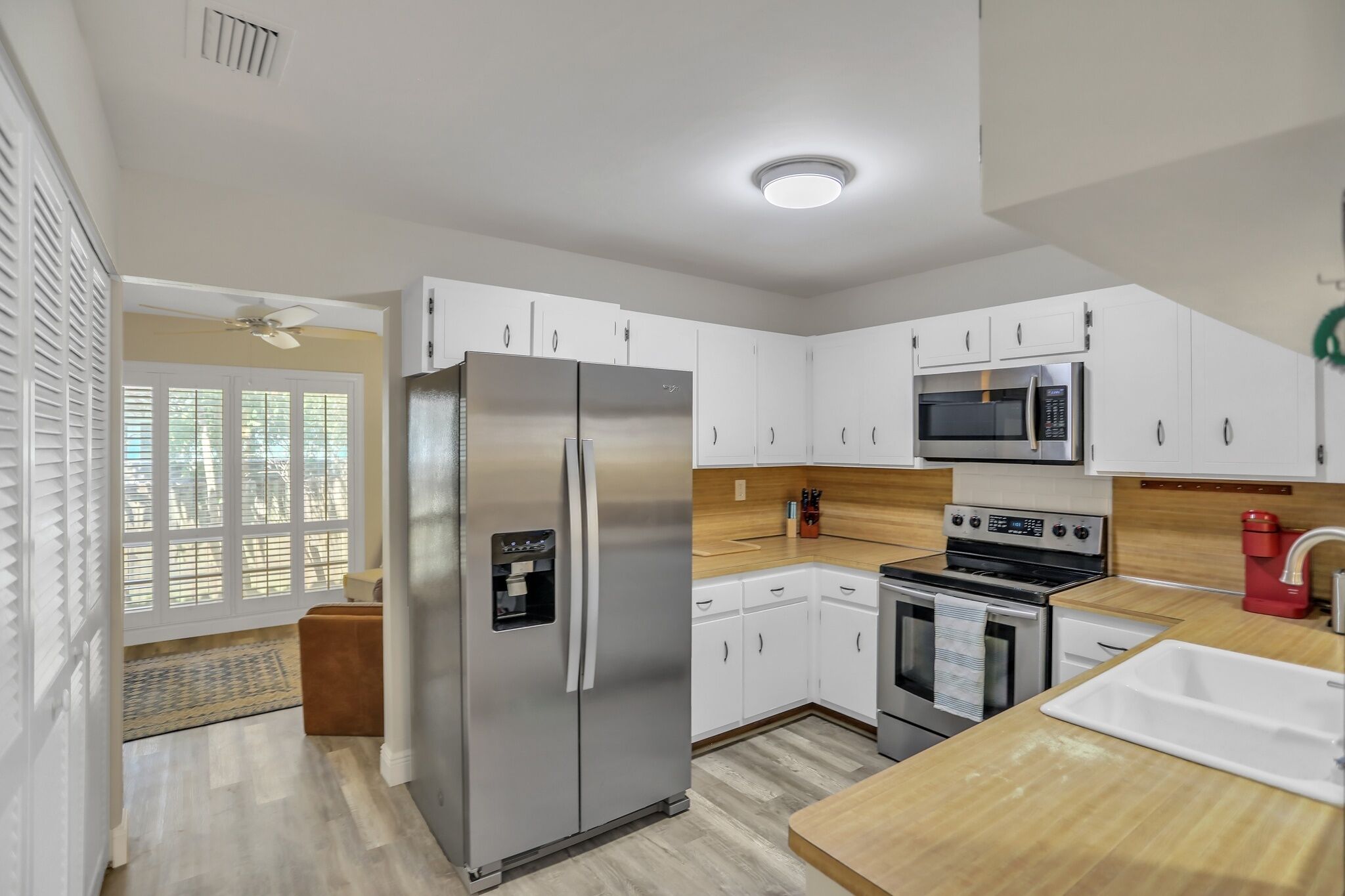 A modern kitchen with white cabinets, stainless steel appliances, and a wooden countertop.