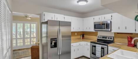 A modern kitchen with white cabinets, stainless steel appliances, and a wooden countertop.