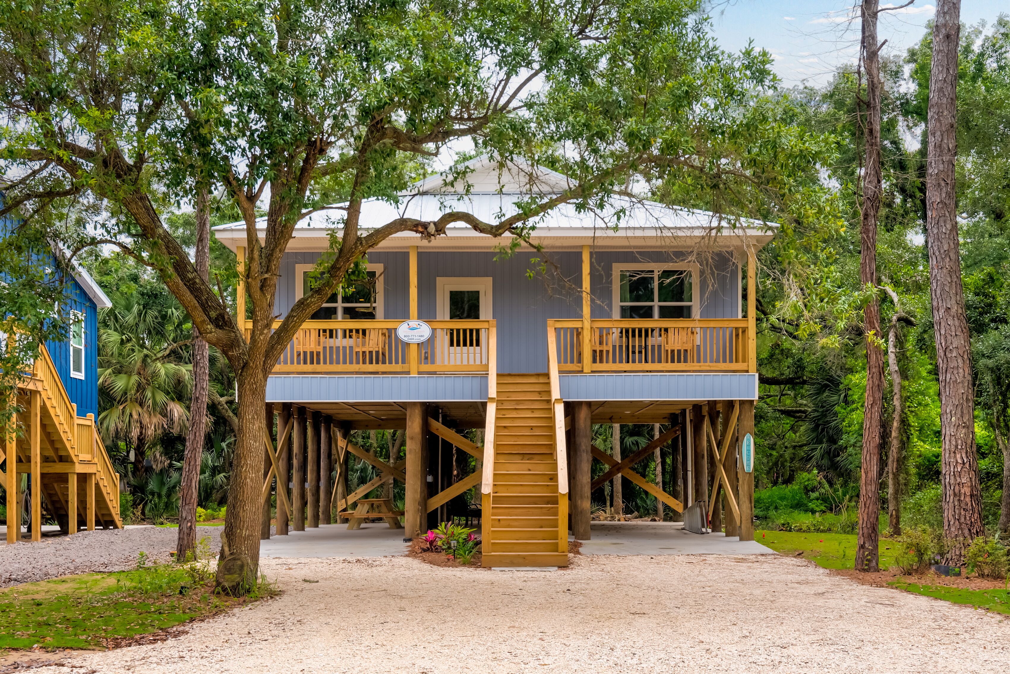A two-story wooden house with a balcony, elevated on stilts, surrounded by trees.