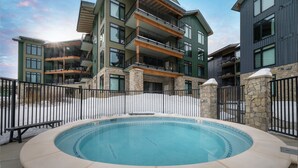 A hot tub surrounded by a stone wall, with a view of multi-story buildings in the background.