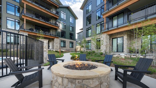 A modern outdoor seating area with a stone fire pit surrounded by Adirondack chairs.