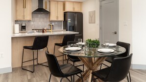 A modern kitchen with wooden cabinets, a stainless steel refrigerator, and a dining area with a glass table and black chairs.