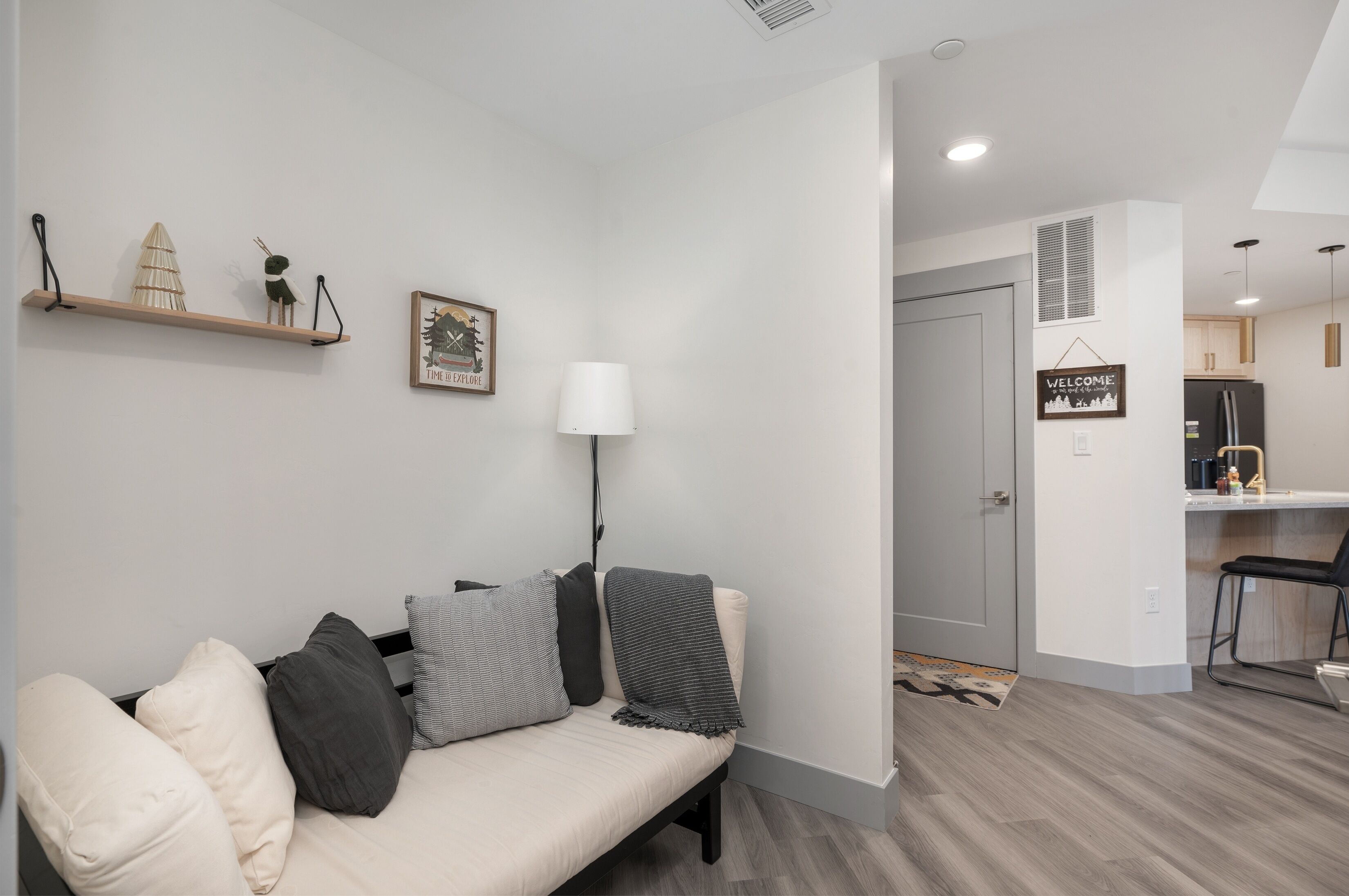 A modern living room with a sofa, pillows, a lamp, and a wall-mounted shelf with decorative items.