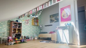 Een kinderspeelkamer met een boekenkast, speelgoed, een ventilator en een bed.