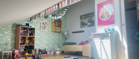 A child's playroom with a bookshelf, toys, a fan, and a bed.