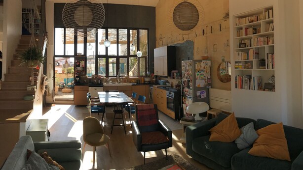 Een ruime woonkamer met een eettafel, diverse stoelen, een bank en een boekenkast.