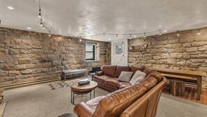 A cozy living room with a stone wall, leather sofa, and a wooden bench. - Modern 2BR Steps from Main St! (Park City)
