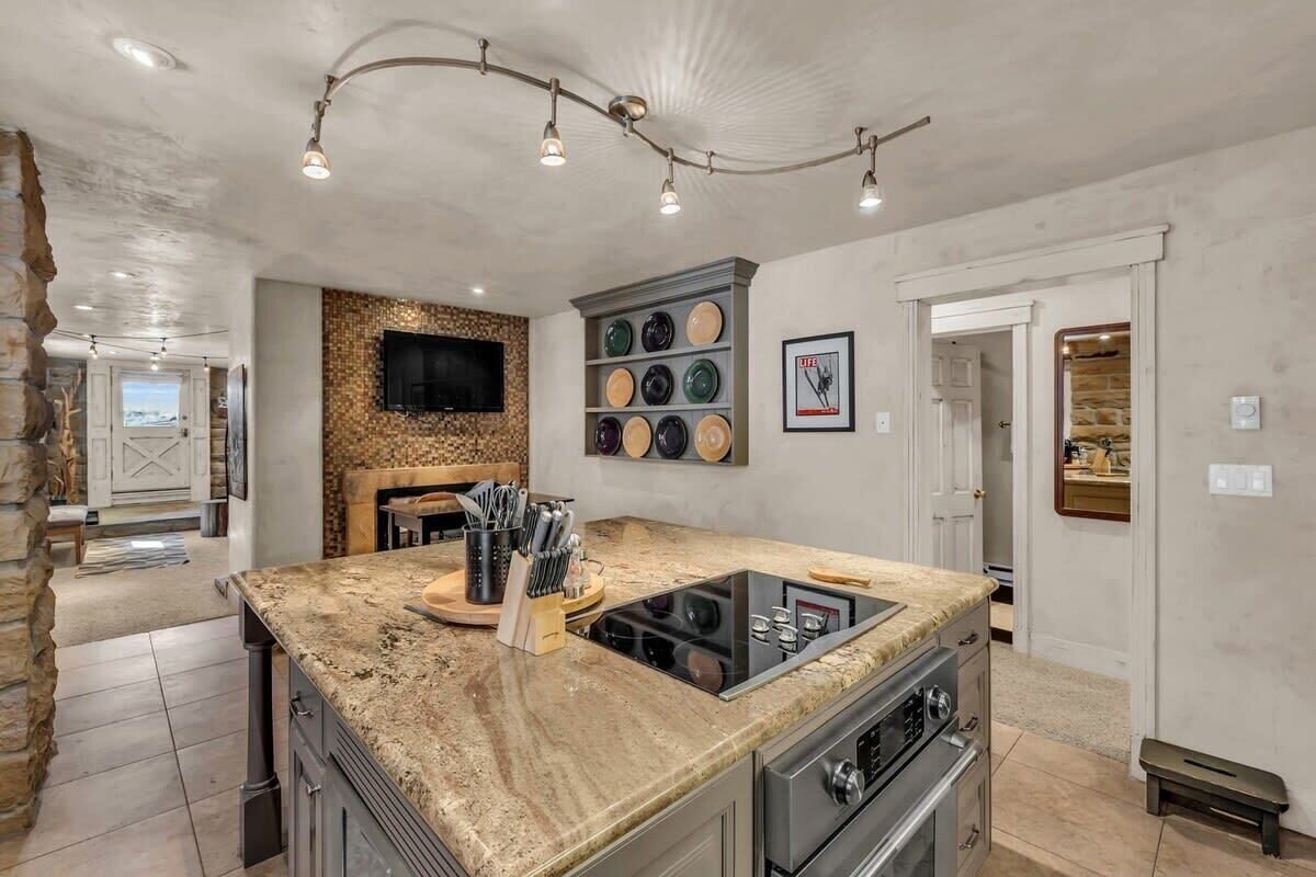 A kitchen with a granite countertop, built-in stove, and a wall-mounted TV.