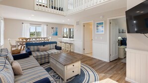 A spacious living room with a high ceiling, a staircase, and a dining area with a table and chairs. - New Beginnings: Fisherman's Paradise | Boat Dock (Nags Head)