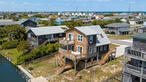 A waterfront property with a dock, a large wooden deck, and a two-story house with a balcony. - New Beginnings: Fisherman's Paradise | Boat Dock (Nags Head)