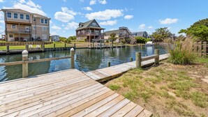 A waterfront property with a dock, a large house with a balcony, and a smaller building with a staircase. - New Beginnings: Fisherman's Paradise | Boat Dock (Nags Head)