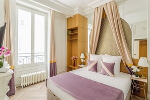 A hotel room with a large bed, a bedside table with a lamp, a nightstand, a wardrobe, a radiator, and a window with curtains. - Merveil - Luxury Suite -Opera - Volney II (Paris)