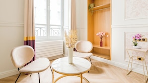 Une pièce comprenant une table ronde, deux chaises, une étagère en bois et une petite table d’appoint sur laquelle se trouve un vase de fleurs.