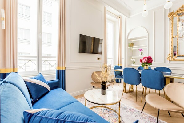 A modern living room with a blue sofa, a round coffee table, and a dining area with blue chairs and a white table.