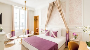 Une chambre d’hôtel avec un lit, un bureau, une chaise, une petite table et une fenêtre avec des rideaux.