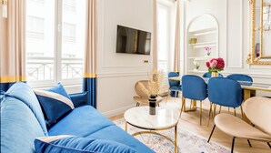 Un salon moderne avec un canapé bleu, une table basse ronde et un coin repas comprenant des chaises bleues et une table blanche.