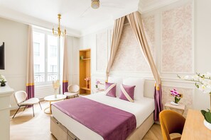 Ein Hotelzimmer mit Bett, Schreibtisch, Stuhl, einem kleinen Tisch und einem Fenster mit Vorhängen.