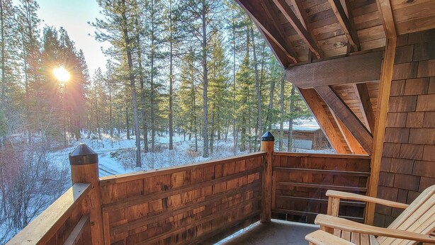 Une terrasse en bois offrant une vue sur une forêt enneigée, avec des chaises en bois et une structure de cabane en bois.