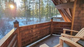 Una terraza de madera con vistas a un bosque nevado, sillas de madera y una estructura de cabaña de madera.