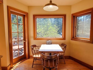 Un comedor con una mesa y sillas, ventanas amplias con vista a árboles, y una lámpara en el techo.