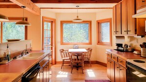 Une cuisine avec des meubles en bois, une table à manger et une fenêtre donnant sur des arbres.
