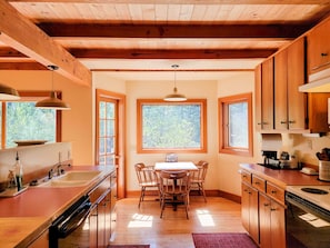 Una cocina con armarios de madera, una mesa de comedor y una ventana con vista a árboles.